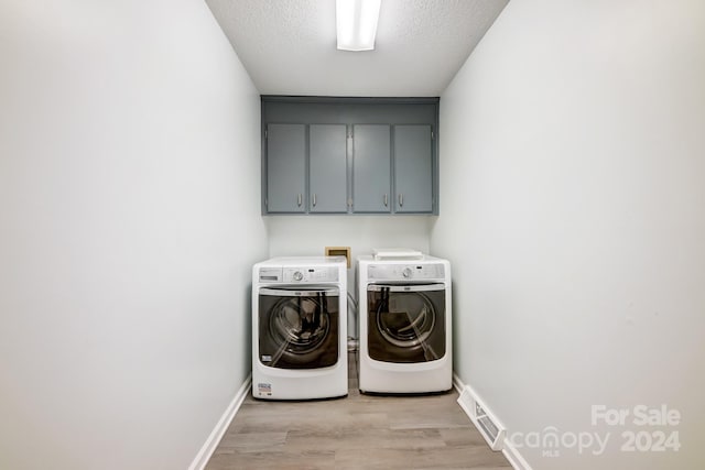 laundry room with independent washer and dryer, cabinets, a textured ceiling, and light wood-type flooring