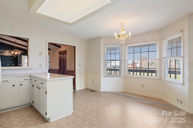 kitchen featuring an inviting chandelier, white cabinetry, kitchen peninsula, hanging light fixtures, and a textured ceiling