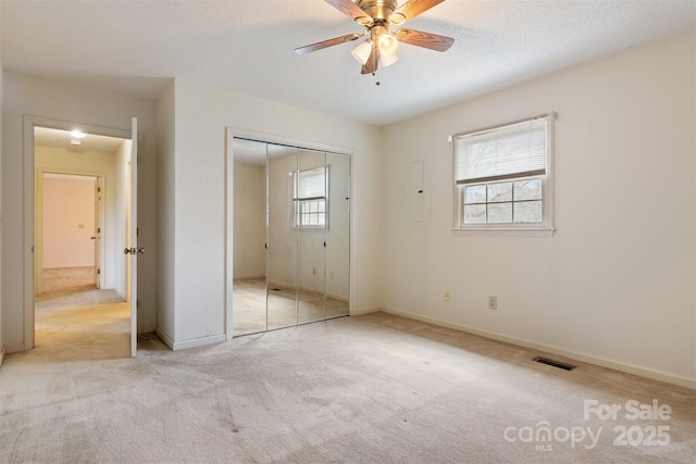 unfurnished bedroom featuring ceiling fan, light colored carpet, a textured ceiling, and a closet