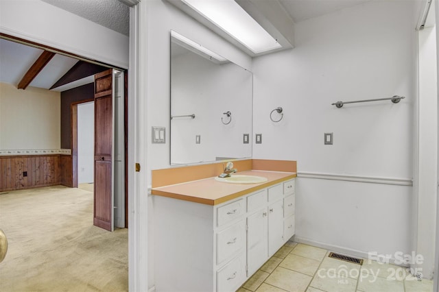 bathroom with a textured ceiling, vanity, lofted ceiling with beams, and wooden walls