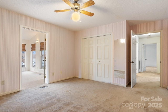 unfurnished bedroom featuring ceiling fan, light colored carpet, a closet, and a textured ceiling