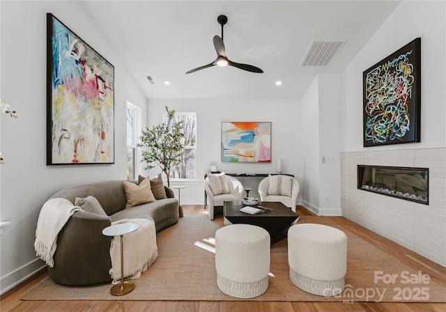 living room featuring hardwood / wood-style flooring, ceiling fan, and a tiled fireplace