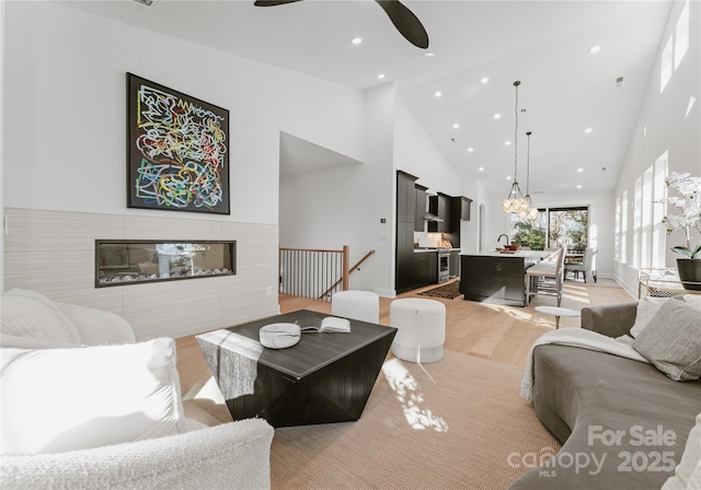 living room with ceiling fan, a towering ceiling, and light hardwood / wood-style floors