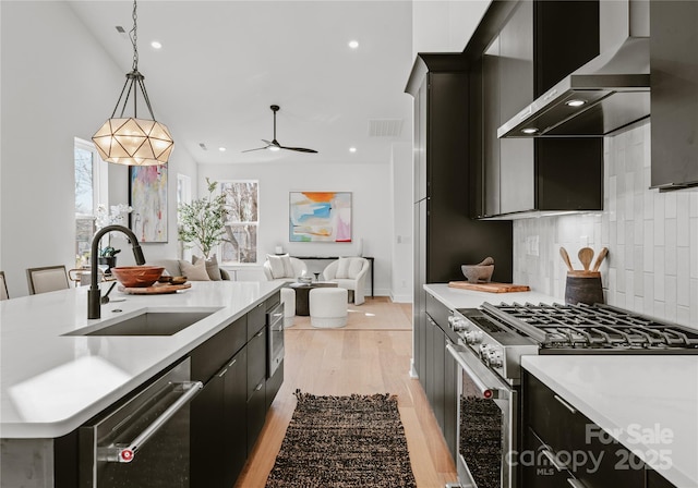 kitchen with sink, wall chimney range hood, pendant lighting, decorative backsplash, and appliances with stainless steel finishes