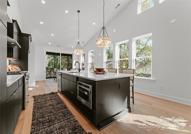 kitchen with a large island, sink, stainless steel gas range oven, pendant lighting, and light hardwood / wood-style floors