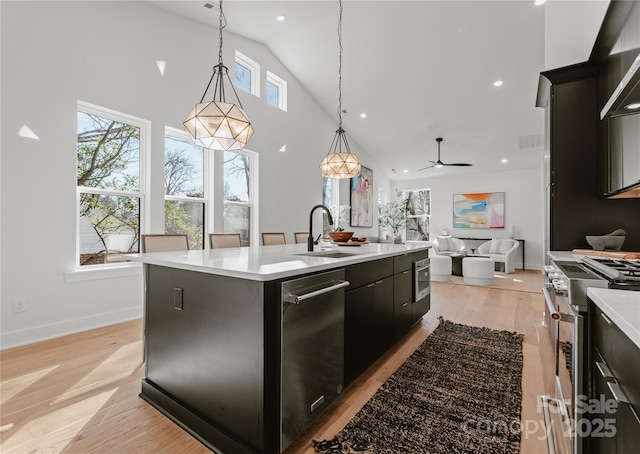 kitchen featuring appliances with stainless steel finishes, ceiling fan, sink, hanging light fixtures, and an island with sink