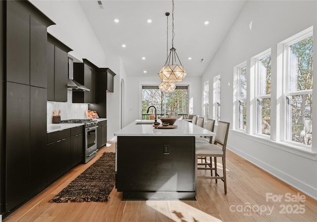 kitchen featuring pendant lighting, high end stainless steel range oven, sink, an island with sink, and a kitchen bar