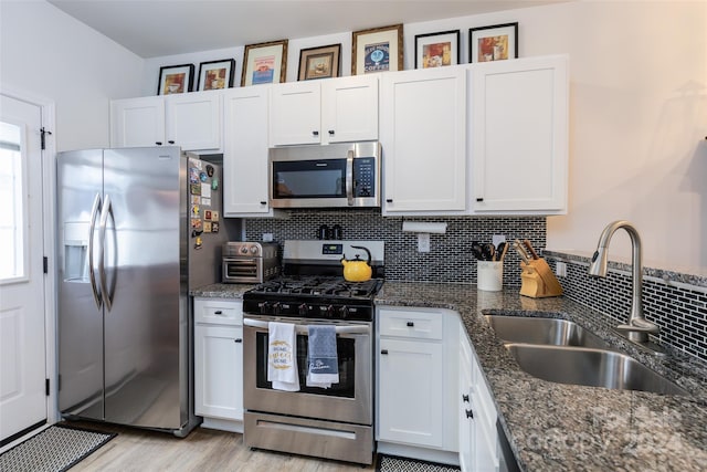 kitchen featuring light wood-type flooring, stainless steel appliances, sink, dark stone countertops, and white cabinetry