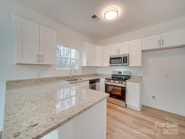 kitchen featuring white cabinetry, light hardwood / wood-style floors, appliances with stainless steel finishes, light stone countertops, and sink