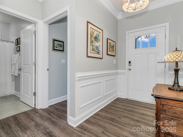 foyer entrance featuring ornamental molding, dark wood-type flooring, and an inviting chandelier