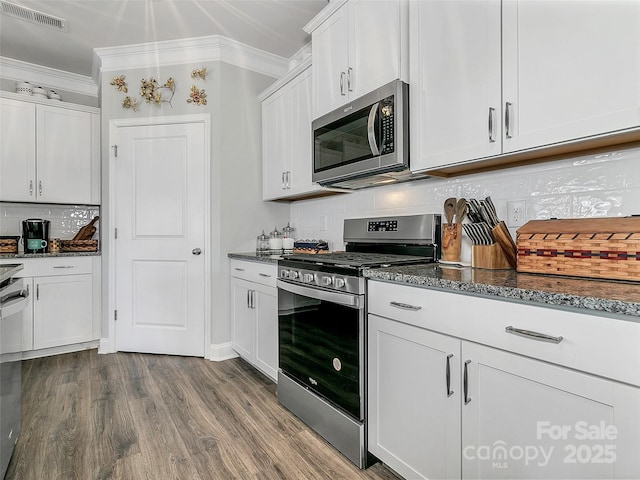 kitchen featuring white cabinetry, appliances with stainless steel finishes, ornamental molding, and dark stone countertops