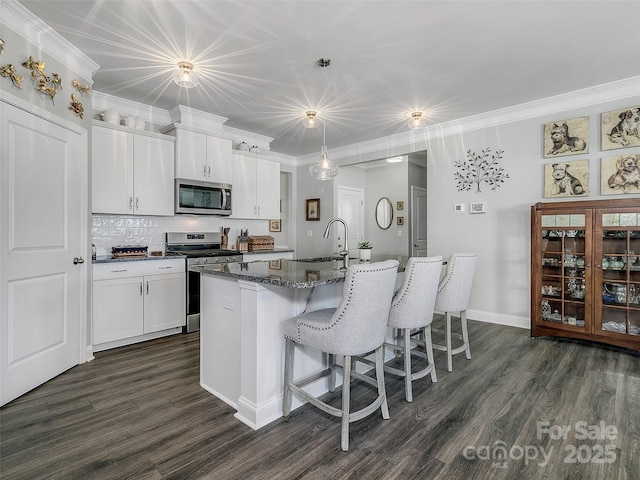 kitchen featuring white cabinetry, stainless steel appliances, an island with sink, and hanging light fixtures