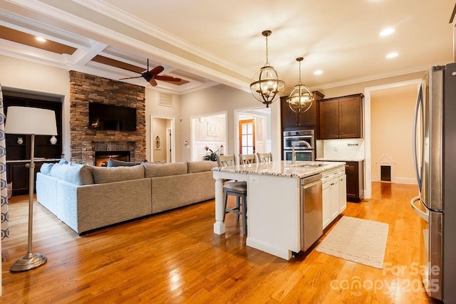 kitchen featuring stainless steel appliances, a stone fireplace, light stone counters, an island with sink, and a breakfast bar area