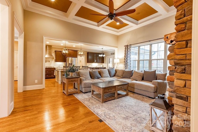 living room with ceiling fan with notable chandelier, light hardwood / wood-style floors, coffered ceiling, and ornamental molding