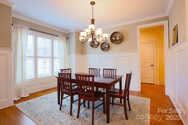 dining area with hardwood / wood-style floors, ornamental molding, and a notable chandelier