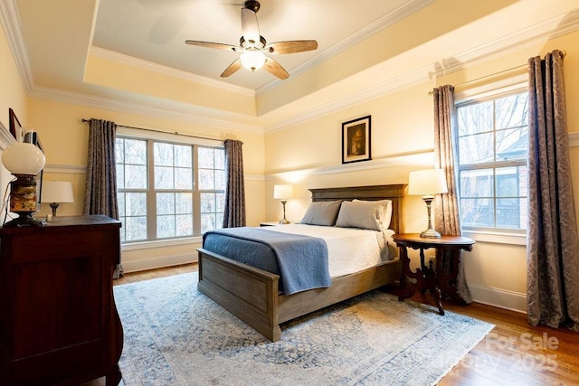 bedroom with multiple windows, a tray ceiling, light hardwood / wood-style flooring, and ceiling fan