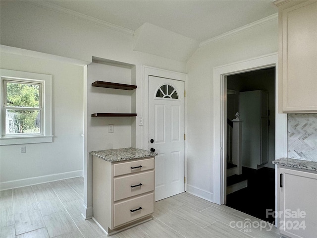 kitchen featuring tasteful backsplash, light stone counters, ornamental molding, light hardwood / wood-style flooring, and white cabinets