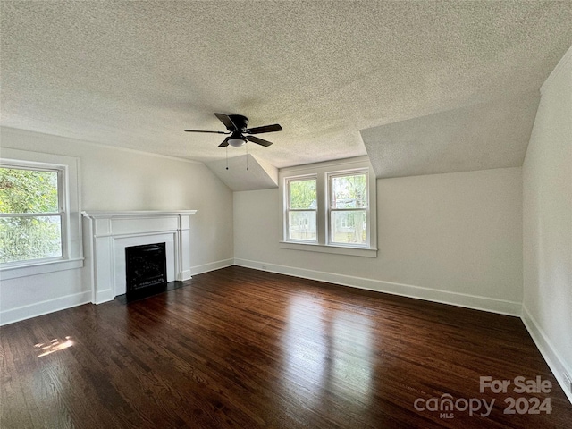 unfurnished living room featuring plenty of natural light, dark hardwood / wood-style flooring, a textured ceiling, and vaulted ceiling