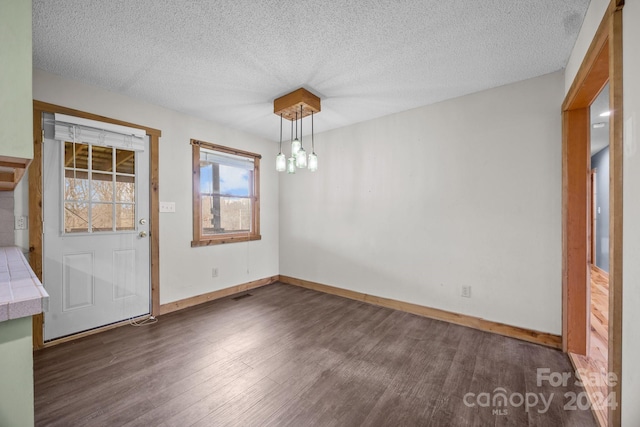 unfurnished dining area featuring a textured ceiling, dark hardwood / wood-style flooring, and an inviting chandelier