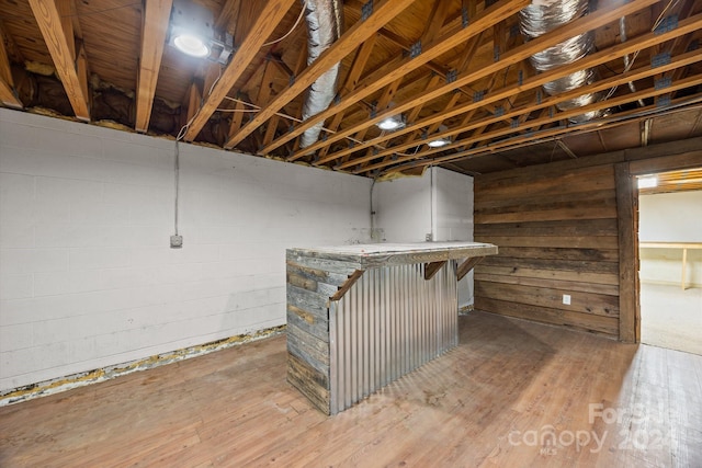 basement with wood walls, indoor bar, and hardwood / wood-style flooring