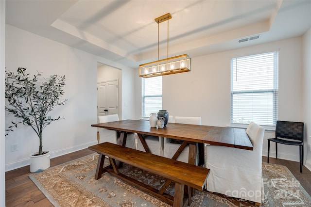 dining room with dark wood-type flooring and a tray ceiling