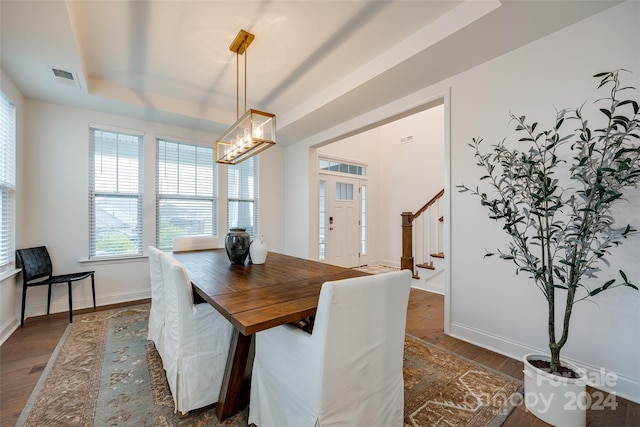 dining space with a chandelier, dark hardwood / wood-style floors, and a tray ceiling