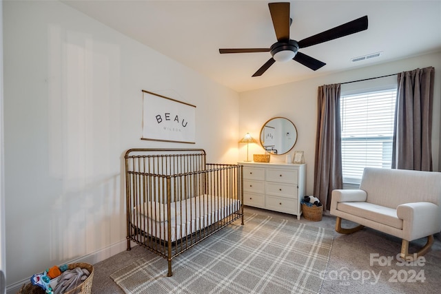 carpeted bedroom with ceiling fan and a crib