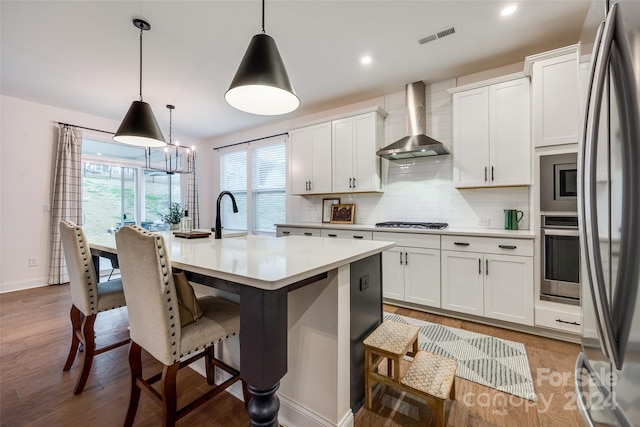 kitchen featuring white cabinets, decorative light fixtures, wall chimney range hood, and appliances with stainless steel finishes