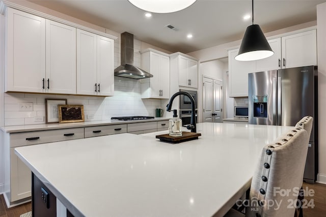 kitchen featuring dark hardwood / wood-style flooring, wall chimney range hood, an island with sink, and appliances with stainless steel finishes