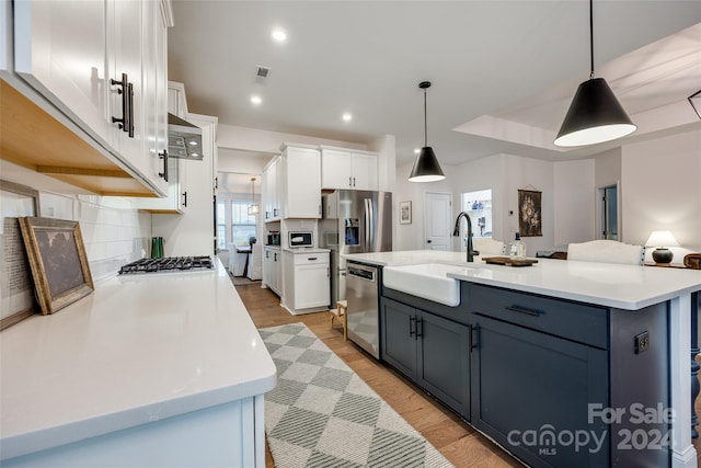 kitchen with white cabinetry, stainless steel appliances, hanging light fixtures, and an island with sink