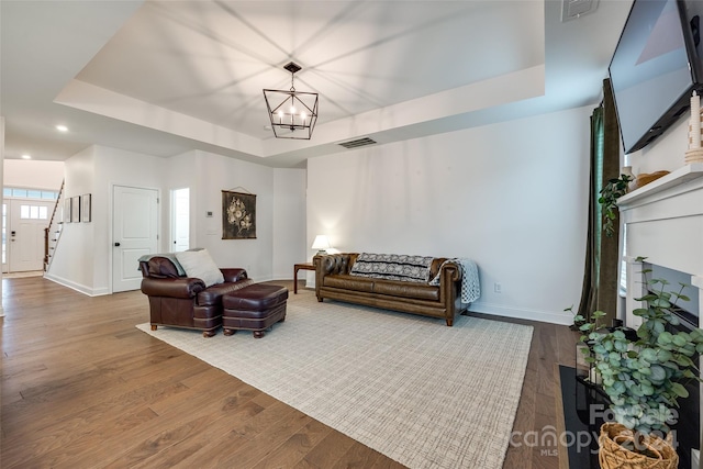 living room with hardwood / wood-style flooring, a raised ceiling, and a notable chandelier