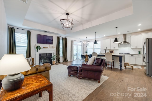 living room featuring light wood-type flooring, a tray ceiling, and a wealth of natural light