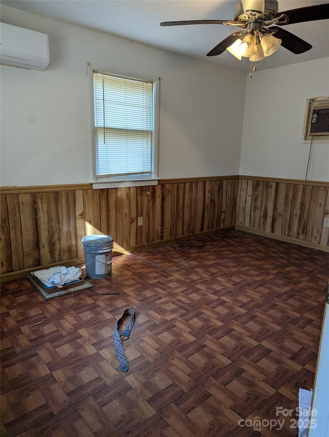 unfurnished room featuring dark parquet flooring, wood walls, a textured ceiling, an AC wall unit, and ceiling fan