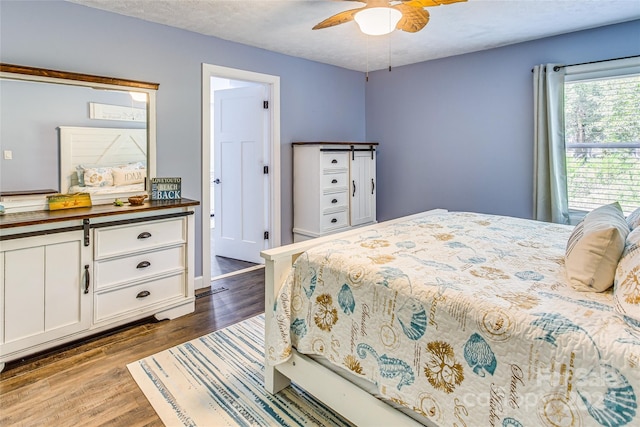 bedroom featuring a textured ceiling, a barn door, ceiling fan, and dark wood-type flooring