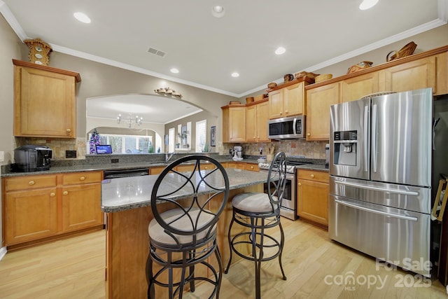 kitchen featuring a kitchen breakfast bar, dark stone counters, light hardwood / wood-style floors, kitchen peninsula, and stainless steel appliances