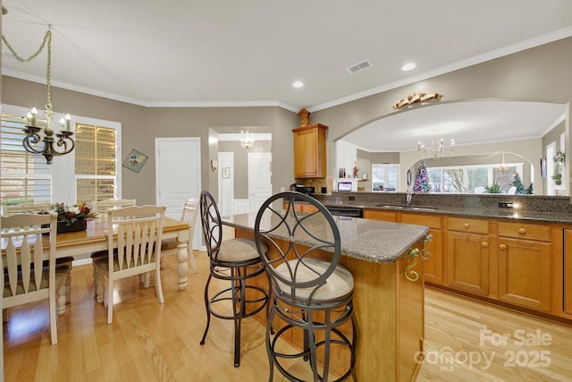 kitchen featuring sink, a chandelier, light hardwood / wood-style flooring, a kitchen island, and dark stone counters