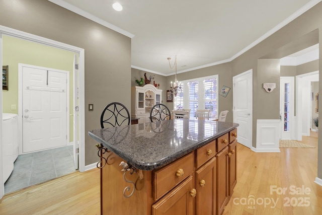 kitchen with ornamental molding, a kitchen island, light hardwood / wood-style floors, and dark stone counters