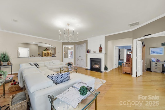 living room featuring ornamental molding, a large fireplace, an inviting chandelier, and light wood-type flooring