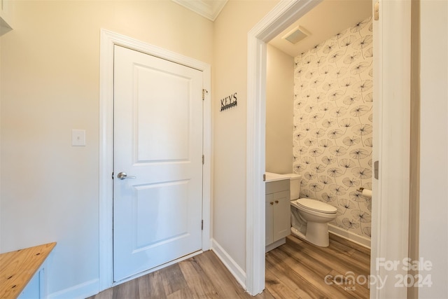 bathroom featuring toilet, vanity, wood-type flooring, and ornamental molding