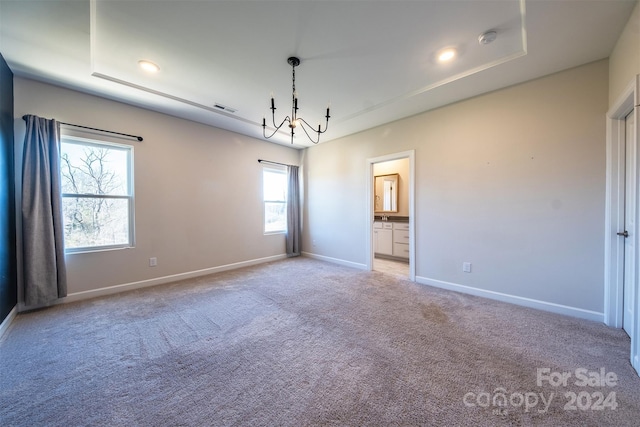 carpeted empty room featuring a raised ceiling, plenty of natural light, and a chandelier