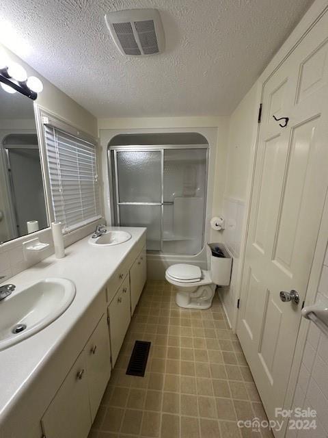 full bathroom featuring vanity, a textured ceiling, toilet, and enclosed tub / shower combo