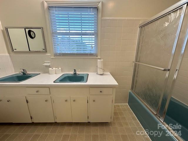 bathroom featuring vanity, tile patterned floors, tile walls, and bath / shower combo with glass door