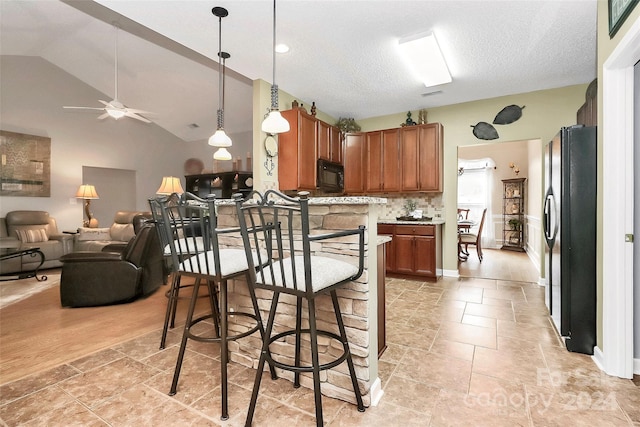 kitchen featuring a breakfast bar, ceiling fan, black appliances, decorative light fixtures, and light hardwood / wood-style flooring