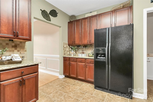 kitchen featuring decorative backsplash, black fridge, light stone countertops, and a textured ceiling