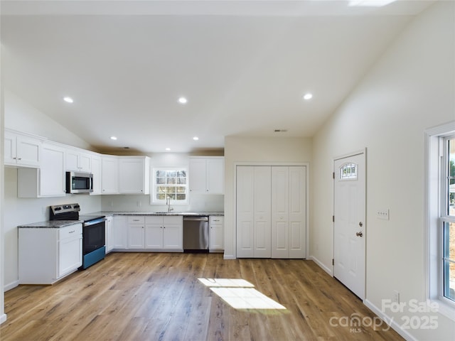 kitchen featuring vaulted ceiling, appliances with stainless steel finishes, plenty of natural light, and white cabinetry