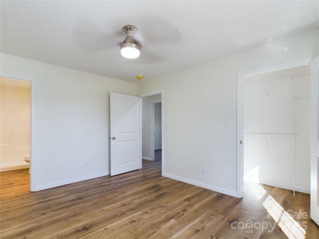 unfurnished bedroom with ensuite bath, a closet, hardwood / wood-style flooring, and ceiling fan