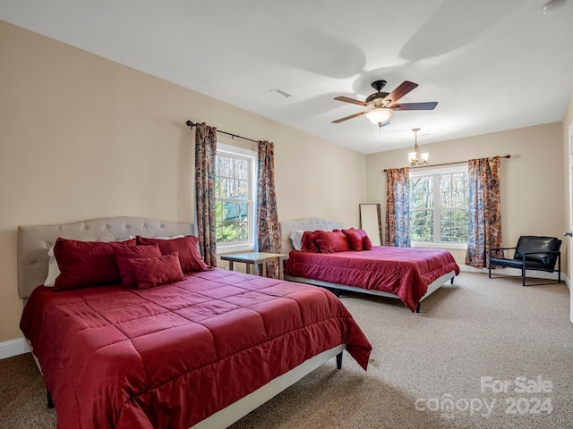 carpeted bedroom featuring multiple windows and ceiling fan with notable chandelier