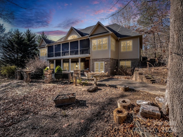 back house at dusk featuring a fire pit, a patio area, and a sunroom