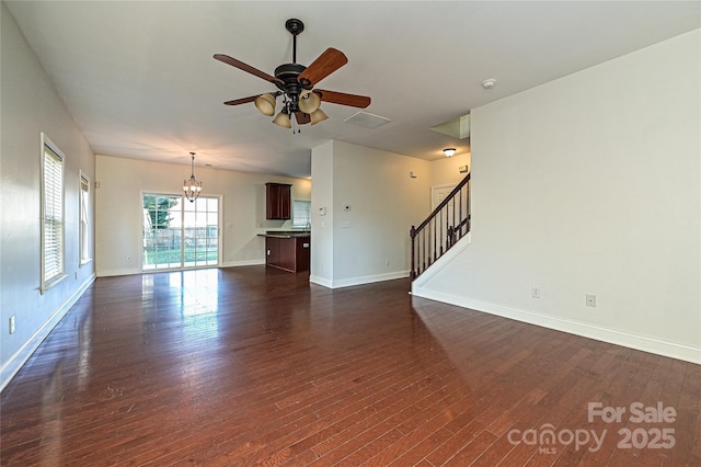 unfurnished living room with ceiling fan with notable chandelier and dark hardwood / wood-style flooring