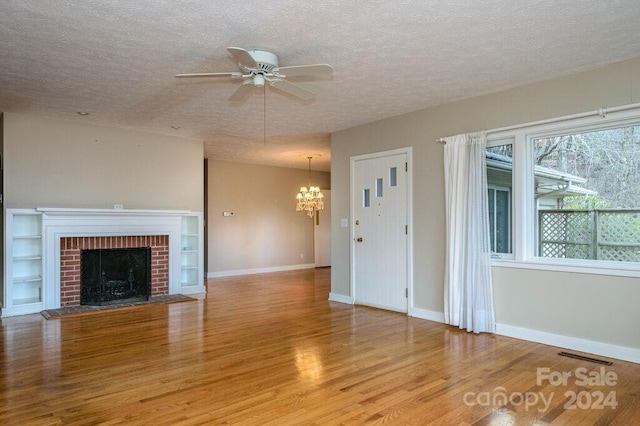 unfurnished living room with a fireplace, light hardwood / wood-style flooring, ceiling fan with notable chandelier, and a textured ceiling